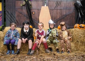Children in Halloween costumes with hay bales and pumpkins at themed hotel event.
