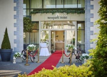 Elegant hotel entrance with red carpet, floral arrangements, and bicycles. Welcoming luxury stay at Newpark Hotel.