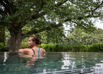 Guest relaxing in serene outdoor pool surrounded by lush greenery and tall trees, offering a peaceful retreat.