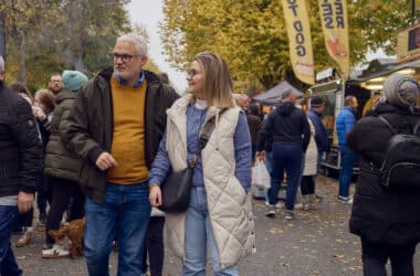 Guests enjoying a lively outdoor market, surrounded by food stalls, autumn trees, and a bustling atmosphere.