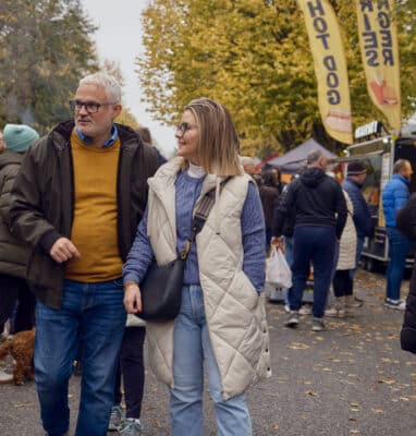 Guests enjoying a lively outdoor market, surrounded by food stalls, autumn trees, and a bustling atmosphere.
