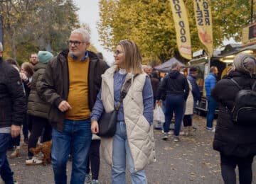 Guests exploring a lively outdoor market with food stalls, surrounded by vibrant autumn trees and a cheerful atmosphere.