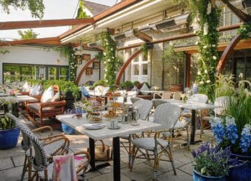 Luxurious hotel terrace with lush greenery, elegant seating, afternoon tea, and vibrant flowers, perfect for relaxation.