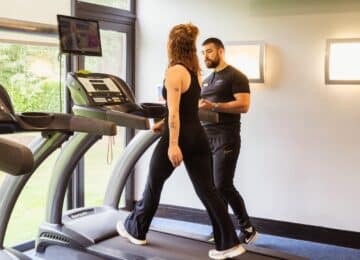 Fitness centre with modern treadmills and large windows, expert personal trainer assisting a guest for a workout.