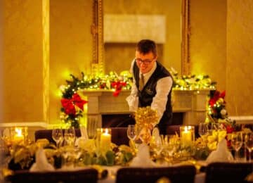 Warm, elegant hotel dining room prepared for a festive celebration with candlelit table setting and attentive service.
