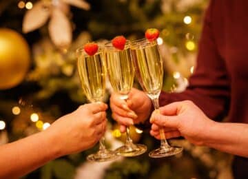 Guests toasting with champagne glasses garnished with strawberries, festive decor in the background for a cosy celebration.