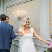 Bride greets wedding guests during an indoor reception at Newpark Hotel Kilkenny, smiling and reaching out to welcome friends in an elegant, softly decorated room.