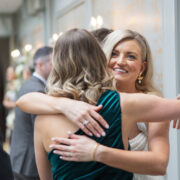 Bride embraces a guest during wedding celebrations indoors at Newpark Hotel Kilkenny, smiling as guests mingle in an elegant, softly lit reception area.