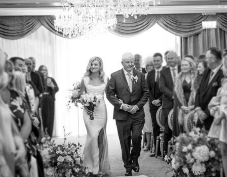 Elegant wedding ceremony in hotel ballroom with chandelier and smiling guests.