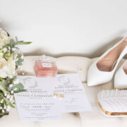 Elegant wedding setup with white roses, stylish invitations, bridal shoes, and pearl clutch, showcasing hotel elegance.