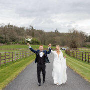 Newlyweds joyfully walk on tree-lined path in lush countryside hotel