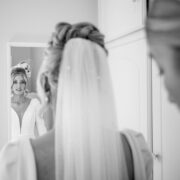 Bride preparing in elegant hotel suite, wearing a white dress and veil, reflected in a mirror. Luxurious wedding venue.