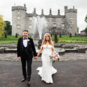 Elegant wedding couple in front of historic castle with fountain, lush gardens, perfect for memorable hotel celebrations.