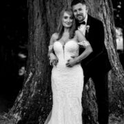 Couple in wedding attire embracing by a large tree at picturesque hotel gardens, perfect for romantic ceremonies.