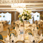 Elegant banquet hall with floral centrepieces, chandeliers, and finely set round tables for luxurious dining experience.