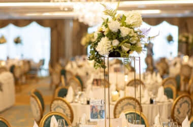 Elegant banquet hall with floral centrepieces, chandeliers, and finely set round tables for luxurious dining experience.