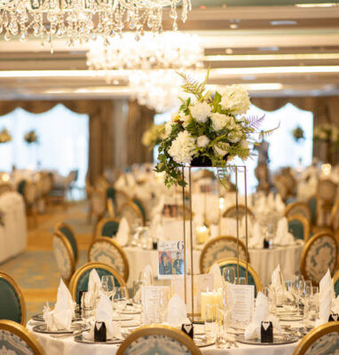 Elegant banquet hall with floral centrepieces, chandeliers, and finely set round tables for luxurious dining experience.