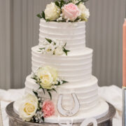 Elegant three-tier wedding cake adorned with pink and white roses, perfect for romantic celebrations at our hotel.