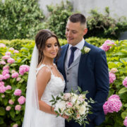 Elegant bride and groom in lush garden surrounded by vibrant pink hydrangeas at upscale hotel.