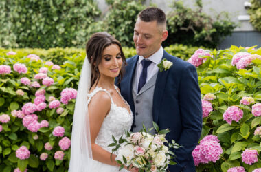 Elegant bride and groom in lush garden surrounded by vibrant pink hydrangeas at upscale hotel.