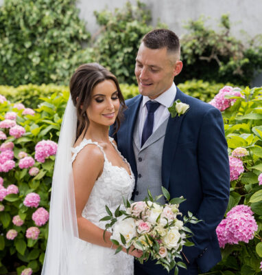 Elegant bride and groom in lush garden surrounded by vibrant pink hydrangeas at upscale hotel.