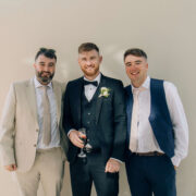 Three smartly dressed guests enjoy drinks at an elegant hotel event, with sunny garden glimpses in the background.