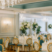 Elegant hotel ballroom with chandeliers, floral arrangements, and ornate dining chairs ready for a luxurious event.