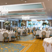 Elegant hotel ballroom with chandeliers, set for a wedding reception with round tables and lavish floral arrangements.
