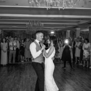 Couple dancing at elegant hotel wedding reception with chandeliers and gathered guests, enjoying luxury event space.