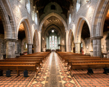 Majestic stone cathedral interior with stained glass windows and wooden pews, offering a tranquil and historic ambience.
