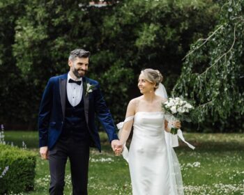 Bride and groom strolling through lush garden at picturesque countryside hotel, perfect for weddings and romantic getaways.