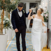 Elegant couple walks through hotel corridor with lush decor, ornate carpets, and ambient lighting, showcasing luxury experience.