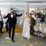 Elegant hotel ballroom wedding celebration with smiling bride and groom, luxury decor, and cheering guests.