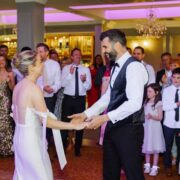 Guests enjoy a lively wedding celebration in a stylish hotel ballroom, adorned with chandeliers and ambient lighting.