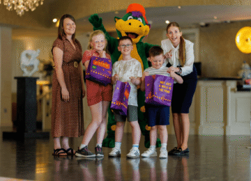 Families enjoying vibrant hotel lobby with friendly mascot and kids' activities. Welcoming atmosphere with engaging staff.