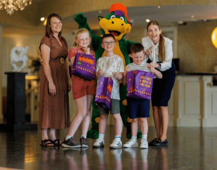 Families enjoying vibrant hotel lobby with friendly mascot and kids' activities. Welcoming atmosphere with engaging staff.