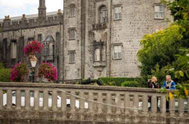 Historic stone castle overlooking river with blooming flowers and people enjoying scenic views. Ideal for romantic getaways.