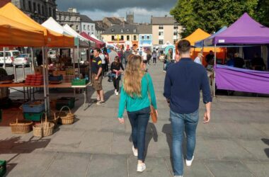 Vibrant market scene with colourful stalls and friendly visitors near charming hotel in scenic city square.