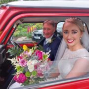 Smiling bride with bouquet in red classic car, capturing joy and elegance at our picturesque hotel wedding venue.