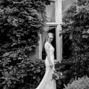 Bridal elegance in lush garden at charming countryside hotel with ivy-covered walls.