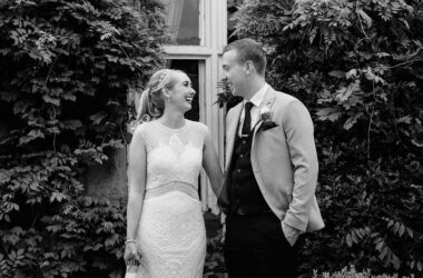 Couple in wedding attire smiling amid lush garden greenery at elegant hotel venue