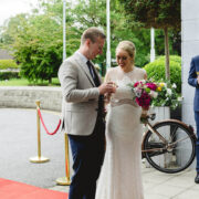 Couple enjoys champagne on red carpet outside elegant hotel with landscaped gardens.