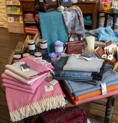 Cosy hotel shop with colourful wool blankets, scented candles, and local artisanal goods on display.