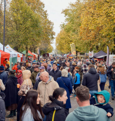Guests enjoy a bustling market with vibrant autumn foliage, showcasing local food stalls