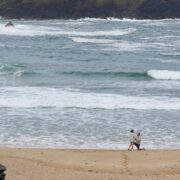 Couple strolling on serene sandy beach with gentle waves, perfect for a tranquil seaside hotel getaway experience.