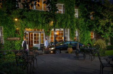 Guests arriving at charming ivy-covered hotel entrance with evening lights and outdoor seating.