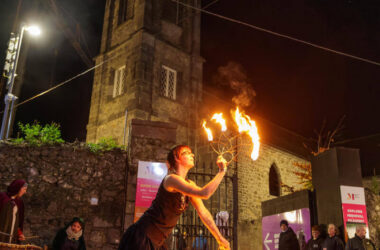 Night fire show at historic hotel courtyard with gothic tower, providing entertainment and cultural experience.